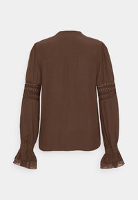 Blouse marron à manches longues avec panneaux en dentelle sur le haut des bras et poignets bordés de dentelle, vue de dos sur fond blanc.
