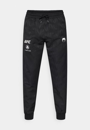 Zwarte joggerbroek met een geometrisch patroon, elastische tailleband, verstelbare trekkkoord en witte bedrukte logo's op de linker dij.