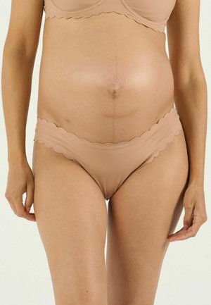 Nahaufnahme des Oberkörpers einer schwangeren Frau, die beiges Unterwäsche-Set mit geschwungenem Rand trägt und ihren runden Bauch betont.