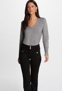 Pull gris à col en V avec des poignets côtelés et des accents de boutons, associé à un jean noir taille haute avec poches avant et boutons décoratifs.