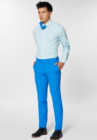 Heledsinine dressipluus, nööbitud, pikad käised. Heledsinised kohandatud püksid. Mustad formaljalatsid detailsete aktsentidega. Minimalistlik taust.