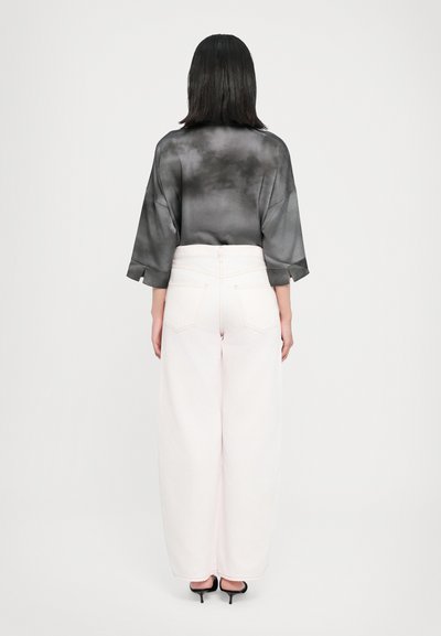 Μαύρο ημιδιαφανές πουκάμισο με μακριά μανίκια και διακριτικό μοτίβο, συνδυασμένο με ψηλόμεσα, ανοιχτό ροζ παντελόνια φαρδιάς γραμμής και μαύρες γόβες.