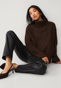 Bruine geribde coltrui gecombineerd met zwarte neplederen broek en donkerbruine slingback hakken. Eenvoudige oorbellen voegen minimale detail toe.