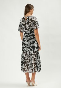 Schwarzes Blumenkleid mit weißen Mustern, transparenter Stoff, Faltärmel und knielange Länge. Verfügt über ein Schlitz-Rückendetail.