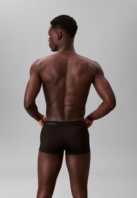 Boxer briefs neri in cotone con un design aderente e dettaglio del logo sulla vita. Il modello è mostrato di spalle, evidenziando la definizione muscolare.