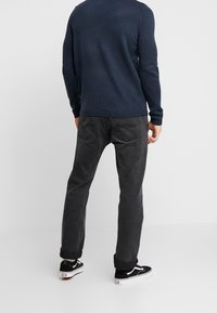 Marineblauer Strickpullover, graue Jeans mit Gesäßtaschen und schwarze Sneaker mit weißen Sohlen. Fokus auf Textur und figurbetontes Design.