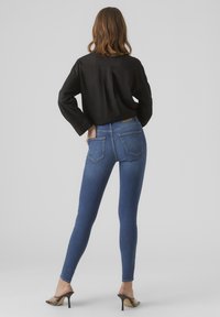 Blå slim fit-jeans med hög midja, synliga bakfickor, tillsammans med en svart långärmad topp. Slät denimtextur, slim fit.