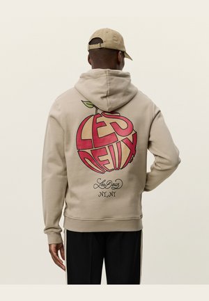 Sudadera crema con un gran gráfico de una manzana roja y el texto "Les Deux" en la parte posterior, con detalles en script negro. Material de algodón suave.
