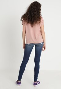 Top corto de manga corta color rosa claro, combinado con jeans ajustados azul oscuro y zapatillas moradas. El top tiene una textura suave y un corte relajado.