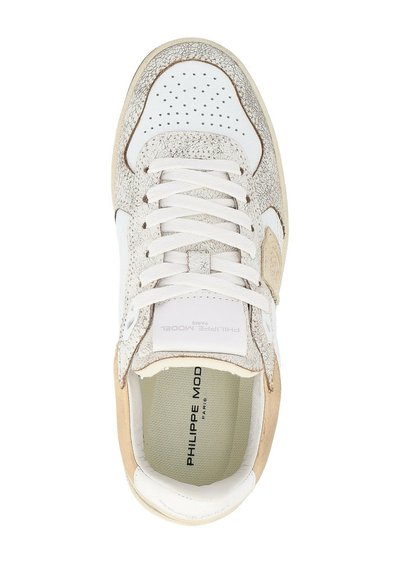 Sneaker bianco con accenti beige testurizzati, punta rotonda, perforazioni sul colletto e lacci piatti. L'interno mostra l'etichetta del marchio e un rivestimento liscio.