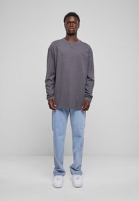 Grå langermet skjorte med rund hals brukt sammen med lyseblå rett bukser og hvite sneakers. Enkelt design, ingen synlige mønstre.
