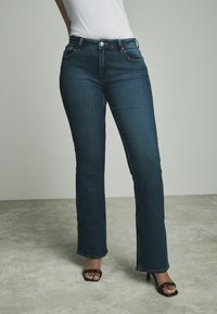Jean en denim bleu foncé à coupe droite avec un design classique à cinq poches, fermeture à bouton en métal et accents de couture subtils.