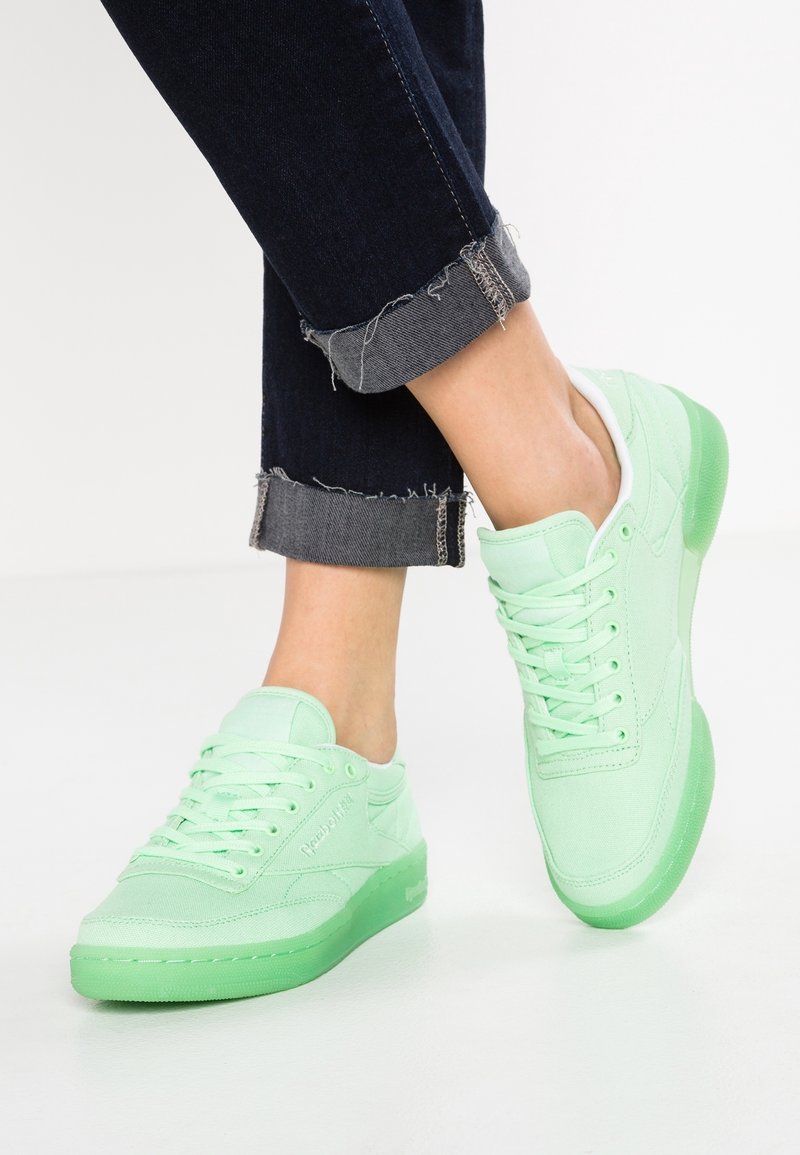 Gröna canvas sneakers med en genomskinlig grön gummisula, med snören och vadderad krage, tillsammans med mörk denimjeans.