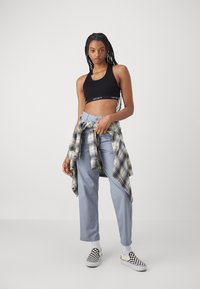 Black cropped tank top, light blue trousers, and a black-and-white plaid shirt tied at the waist. Black-and-white checkered slip-on shoes.