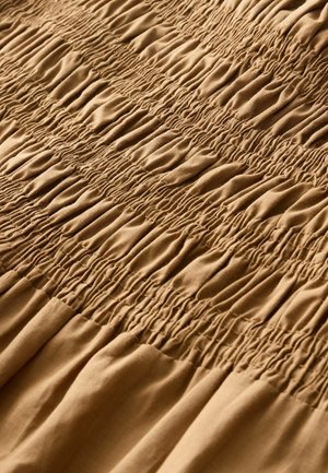 Rudas medžiaga su surinktomis smukimo detalėmis. Minkšta tekstūra su nuosekliais raukiniais, kurie sukuria bangų raštą visame paviršiuje.