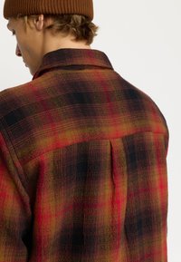 Rood, geel en zwart geruit overhemd met een kraag, voorzien van een achterkant met plooien en textuurstof. Dit shirt benadrukt een ontspannen pasvorm en warme kleuren.