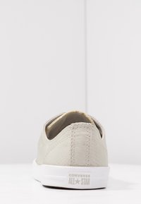 Chaussure à enfiler en toile gris clair avec une finition texturée, semelle en caoutchouc blanche, et accents dorés subtils sur la doublure intérieure. Logo présent sur le talon.