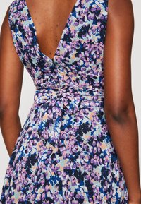 Robe à imprimé floral avec un fond bleu marine, des fleurs roses et bleu clair, un profond décolleté en V dans le dos et une ceinture nouée à la taille.
