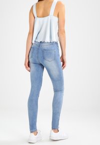 Ljusblå croppad topp med fransig fåll i kombination med ljusblå tajta jeans med bakfickor, bärs med vita sneakers.