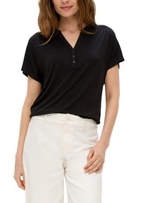 Zwarte korte mouwen top met een V-hals en een drieknoopsluiting, gecombineerd met lichtbeige hoge taille broeken. Zachte, losse pasvorm, minimalistisch ontwerp.