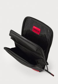 Schwarze Reißverschluss-Geldbörse mit zwei Fächern, ausgestattet mit einem roten "HUGO"-Logo-Tag und einem strukturierten Innenfutter. Aus strapazierfähigem Material mit glatter Oberfläche.