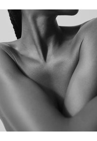 Image en noir et blanc se concentrant de près sur un teint de peau lisse et foncé avec une clavicule et des épaules visibles, mettant en valeur les ombres et les textures.