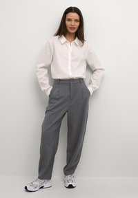Chemise blanche à boutons, pantalon gris ample avec plis et baskets blanches. Design simple avec des textures lisses, sans motifs visibles.