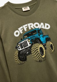 Olijfgroene sweatshirt met een grafische afbeelding van een blauwe off-road voertuig. Grote witte tekst "OFFROAD" erboven. Zachte stof met een ronde hals.