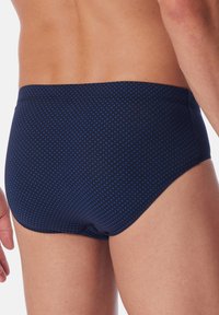 Marineblaue Schwimmslips mit einem kleinen blauen geometrischen Muster, elastischem Bund und einer figurbetonten Passform für Komfort und Unterstützung.