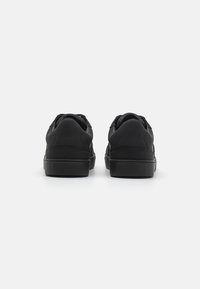 Baskets noires avec une tige en cuir lisse, bout arrondi et semelle en caoutchouc plate. La vue arrière montre un col rembourré et un design minimaliste.