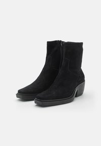 Botas de ante negras hasta el tobillo con puntera afilada, cremallera lateral y tacón ancho para mayor soporte y estabilidad. Textura suave y diseño elegante.