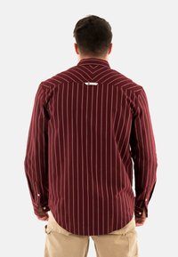 Maglietta a maniche lunghe a righe rosse e bianche con polsini a bottoni e orlo rotondo. Presenta un'etichetta del marchio sulla parte posteriore della spalla. Il tessuto appare texturizzato.