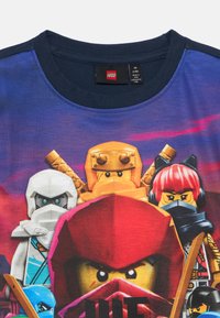 Navyblaue T-Shirt mit einem bunten Grafikdesign von LEGO-Figuren; verfügt über einen runden Ausschnitt und kurze Ärmel, aus weichem Material gefertigt.