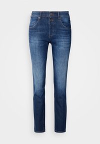 Jean en denim bleu à coupe slim, avec des détails délavés sur les cuisses et les genoux, et deux boutons visibles à l'avant au-dessus de la braguette zippée.