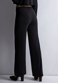 Pantalons larges noirs en matériau doux et extensible avec une taille élastique, présentant une texture lisse et un design longueur sol.