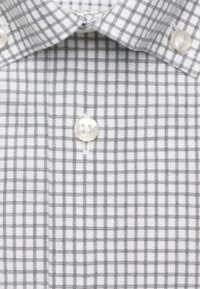 Gros plan d'une chemise blanche avec un motif à carreaux gris, montrant le col et un bouton au centre.