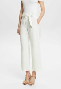 Pantalons larges en lin blanc avec une ceinture nouée �à la taille. Texture lisse et ourlet à la cheville. Portés avec des talons fins de couleur claire.
