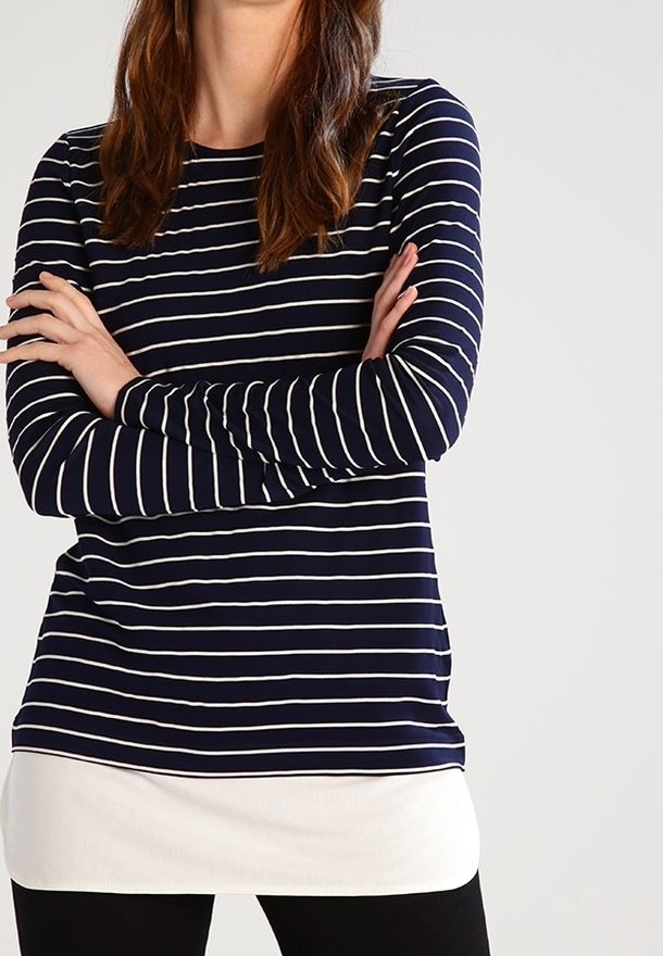 Mörkblå långärmad topp med vita horisontella ränder, med rund halsringning och lager av vit fåll, bärs över svarta leggings.