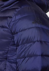 Marineblauwe gewatteerde jas met gestikte secties, glanzende, gladde textuur en een zwart logo op de linkerborst. Met kap.