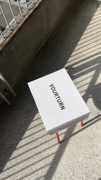 Bílý obdélníkový stůl s červenýma nohama, na jehož vrchní ploše je uprostřed umístěn text "YOURTURN". Text je tučný a bezpatkový.