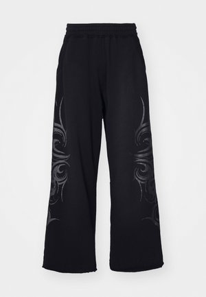 Pantalones de chándal negros con un corte de pierna ancha, que presentan un patrón tribal tonal a lo largo de los lados y una cintura elástica para mayor comodidad.