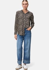 Blouson met luipaardprint, voorzien van een knoopsluiting aan de voorkant en lange mouwen; gecombineerd met lichtblauwe wijde jeans met opgerolde boorden en witte sneakers.
