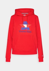 Sweat à capuche rouge avec poche kangourou à l'avant, capuche à cordon réglable, motif étoile bleu et orange, et inscription "Tommy Jeans" sur la poitrine.