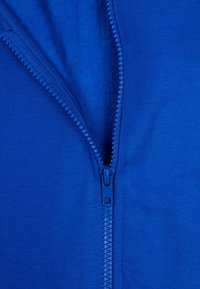 Abbigliamento blu con zip, realizzato in un tessuto testurizzato. La zip è posizionata centralmente, con un cursore liscio e una fila di denti arrotondati.