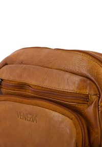Brązowa skórzana torba z dwoma widocznymi kieszeniami na zamek i napisem "VENEZIA" wytłoczonym na przedniej kieszeni.