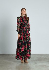 Zwarte maxi-jurk met lange, opgeblazen mouwen en een hoge hals, voorzien van een bloemenpatroon in rood en groen. Gelaagd stof met een gerimpelde zoom.