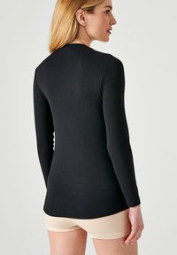 Top nero a maniche lunghe con silhouette aderente, realizzato in tessuto morbido, con scollo tondo e texture delicata, indossato con pantaloni corti nudi.