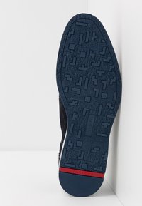 Semelle de basket bleu marine avec motif de grip en caoutchouc texturé, présentant des formes géométriques en relief et un accent rouge au talon.