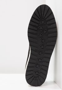 Sole di scarpa in gomma nera con un profondo motivo di battistrada. Presenta una superficie texturizzata e una forma arrotondata con dettagli bianchi ai bordi.