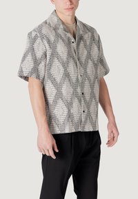 Camicia a maniche corte in un tessuto crema chiaro con motivo a rombi neri, con chiusura a bottoni e vestibilità comoda.